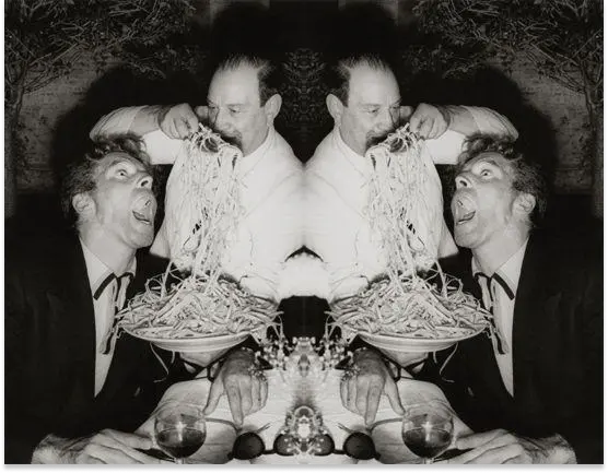 A black and white photo of a man in a suit sitting at a table. His mouth is stretched wide open, and another main is scooping up spaghetti with a fork, to shove into the first man's mouth. The photo has been duplicated (copied), flipped horizontally, and placed next to the original photo, resulting in a fractally mirrored effect.
