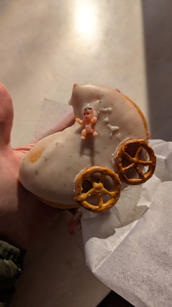 A donut made to look like a baby carriage, with circular pretzel wheels and a small plastic baby doll stuck in it. From Dottie's Donuts in Philly. click for full resolution.