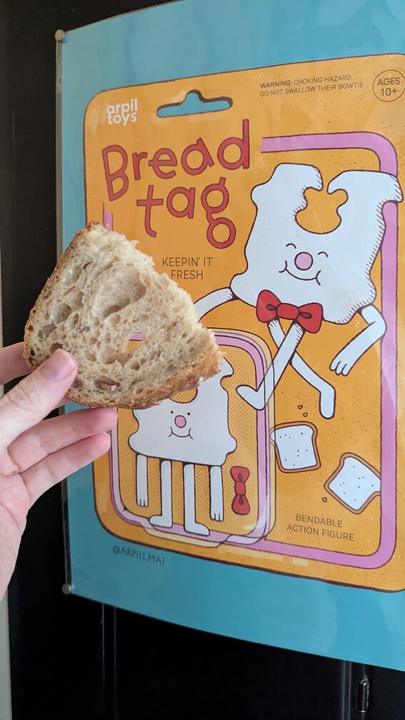 A poster celebrating a fictional children's toy modeled after the Bread tags you get that hold a plastic bag of bread closed. I'm holding up a slice of bread next to it. click for full resolution.