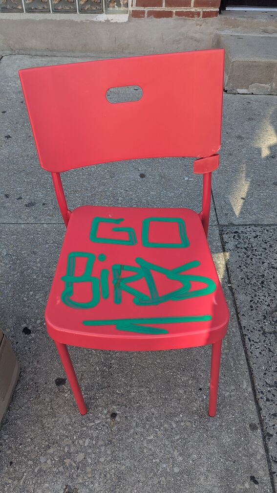 A red plastic chair on a sidewalk with the words 'Go Birds' painted on the seat click for full resolution.