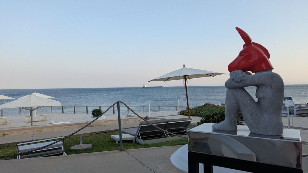 A strange statue of a sitting woman, her arms around her knees, with a red jackal's head. Overlooks a beautiful ocean. From a bougie hotel in Cascais that I got a drink at one time. click for full resolution.