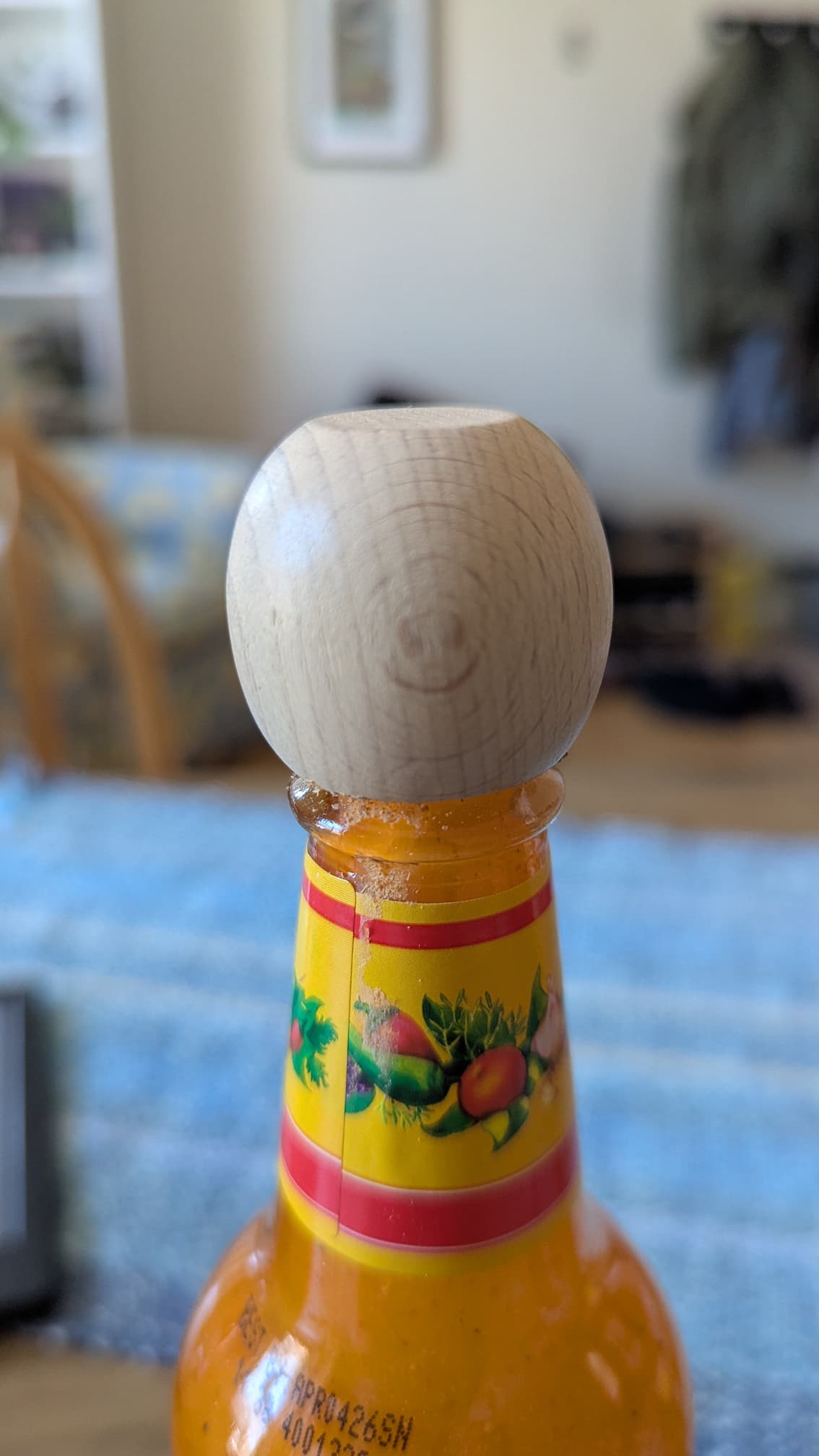 A cholula bottle with a spherical wooden cao. The wood grain of the cap has what looks like a little smiley face on it.
