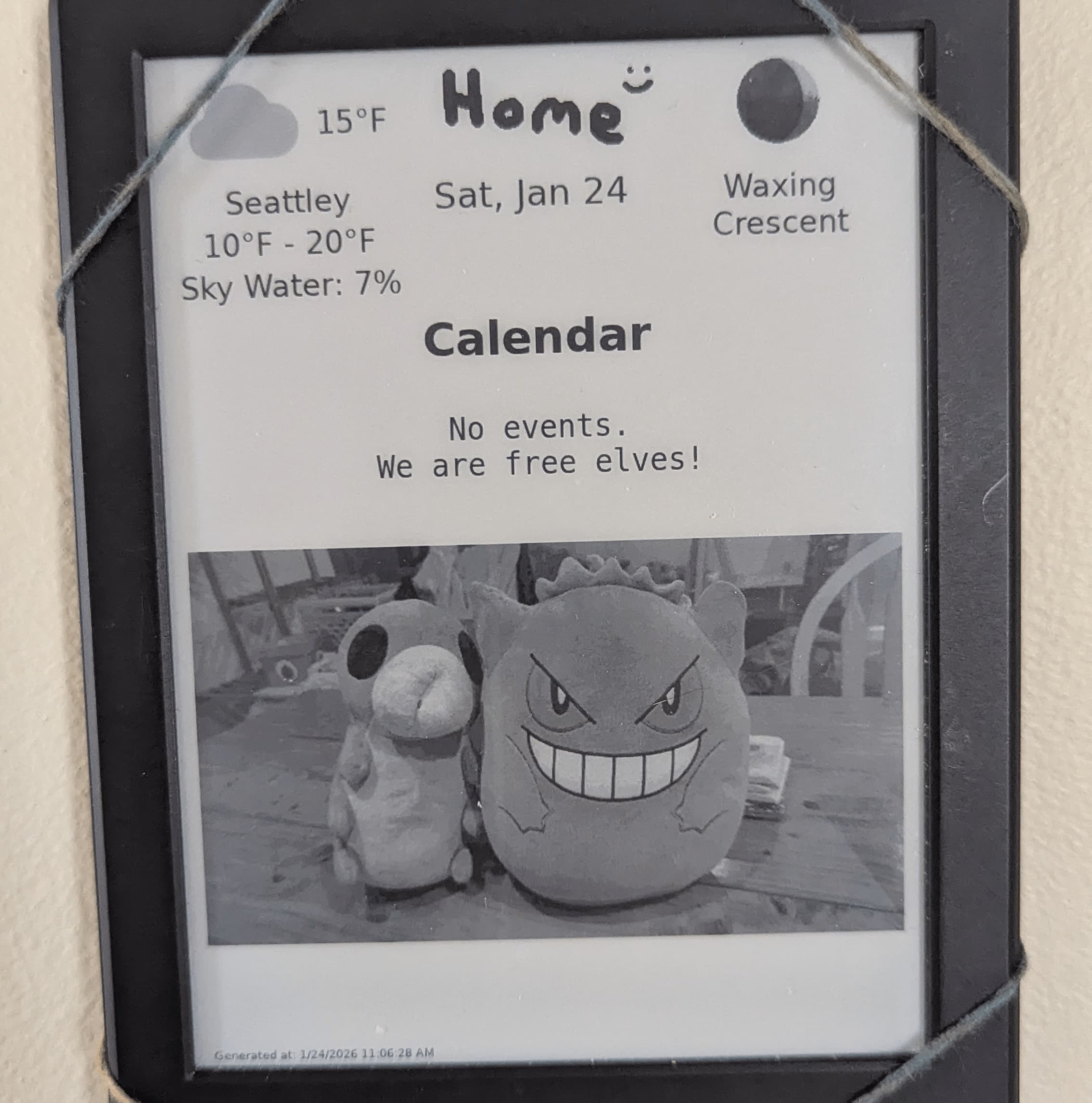 A picture of my kindle wall display when there's no events in the calendar. The display is rendered in three rows: the first with the weather, current date, and moonphase. The second has the empty calendar with the message 'No events. We are free elves.' The third row has a photo of some stuffed animals (the grub from Hollow Knight and Gengar from Pokemon).