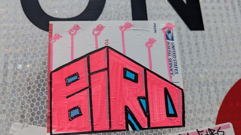 A graffiti slap sticker drawn in marker on a blank USPS postal sticker. Has the stylized word 'Bird' drawn in pink ink with some cartoon flamingos growing out of it. click for full resolution.