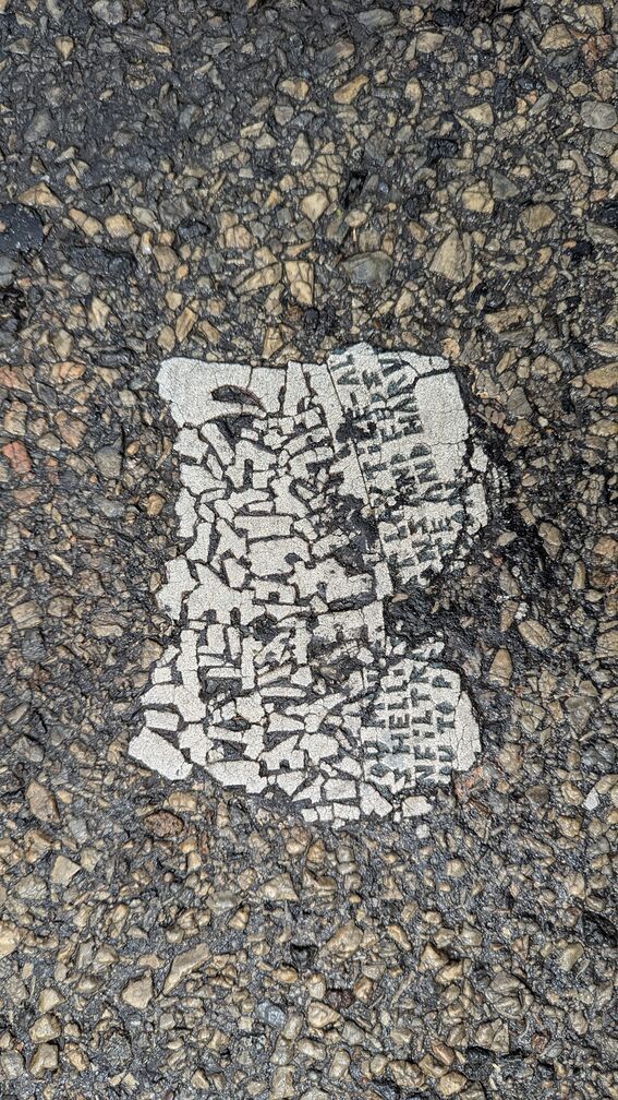 A cermaic tile implanted in the asphalt of a city street. The text is mostly impossible to make out. click for full resolution.