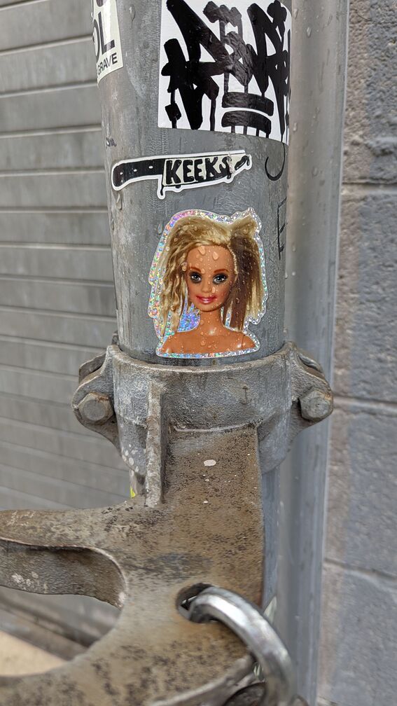 Three stickers: a tag I can't read, a Keeks sticker with the name printed on a graphic of a knife, and then an illustration of a crying barbie doll with eyeliner. click for full resolution.