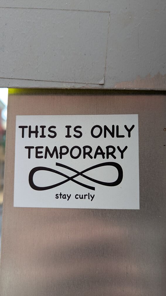A printed sticker with the words 'This is only temporary. Stay Curly.' There's also a curly symbol almost like an infinity sign in the middle of the sticker. This is curly's symbol which will show up in future stickers. click for full resolution.