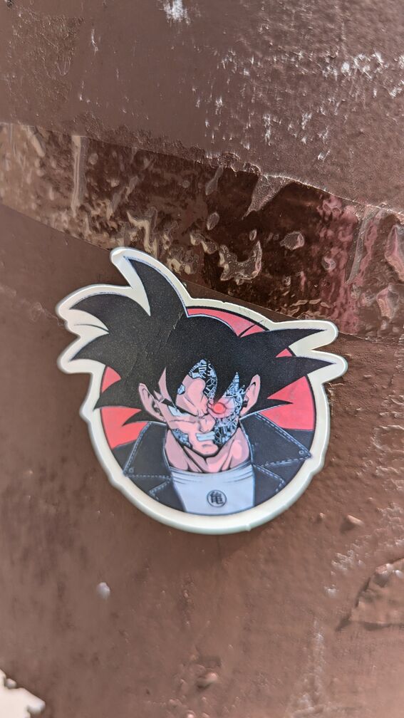 A sticker of a cyborg looking Goku from Dragon Ball Z, with bits of metal poking through under his face. click for full resolution.