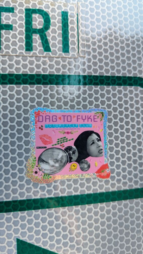 A colorful shiny sticker that reads: Dag To Fyke Motocycle Club. Has a collection of random images, including a woman gazing to the side and a motorcycle lamp bulb. click for full resolution.