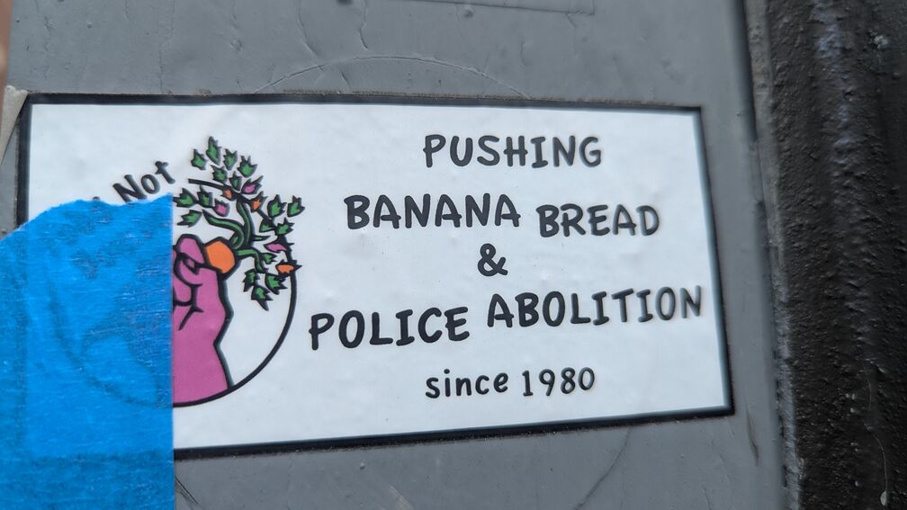 A Food Not Bombs sticker that says: Pushing Banana Bread & Police Abolition since 1980 click for full resolution.