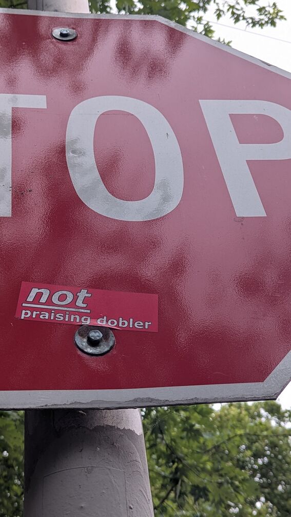 A Stop sign with a red sticker pasted below the word Stop, so the whole sign reads: Stop not praising dobler click for full resolution.