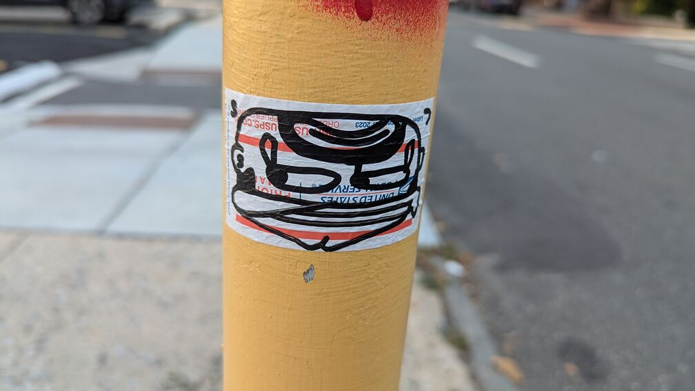 A slap of a cartoonish male face, upside down on a pole. His eyes look shiftily to one side. click for full resolution.