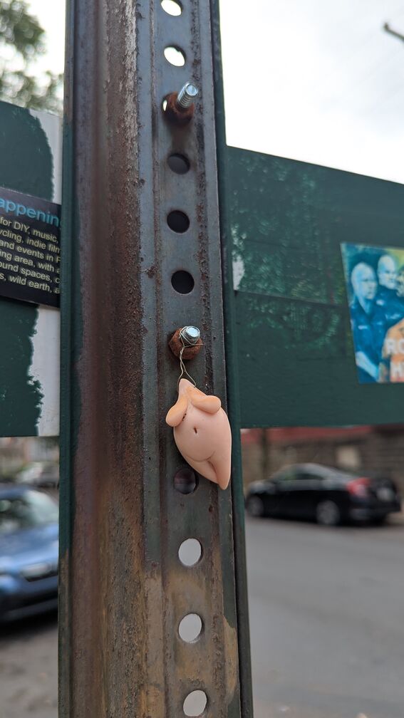 A plastic figurine of the torso of a fem body, attached to a street sign. click for full resolution.