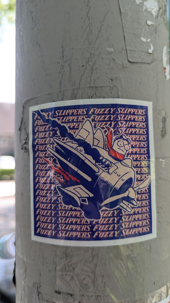 A sticker with a cartoony figure in an old timey war plane. The words Fuzzy Slippers are repeated behind the drawing. click for full resolution.