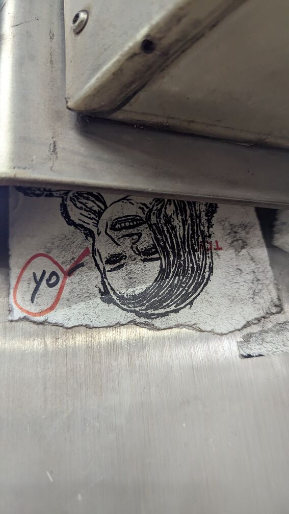 A sticker of the shrock lady from before, upside down under a sign. Somebody has sharpied the word 'yo' rightside up in a speech bubble. click for full resolution.