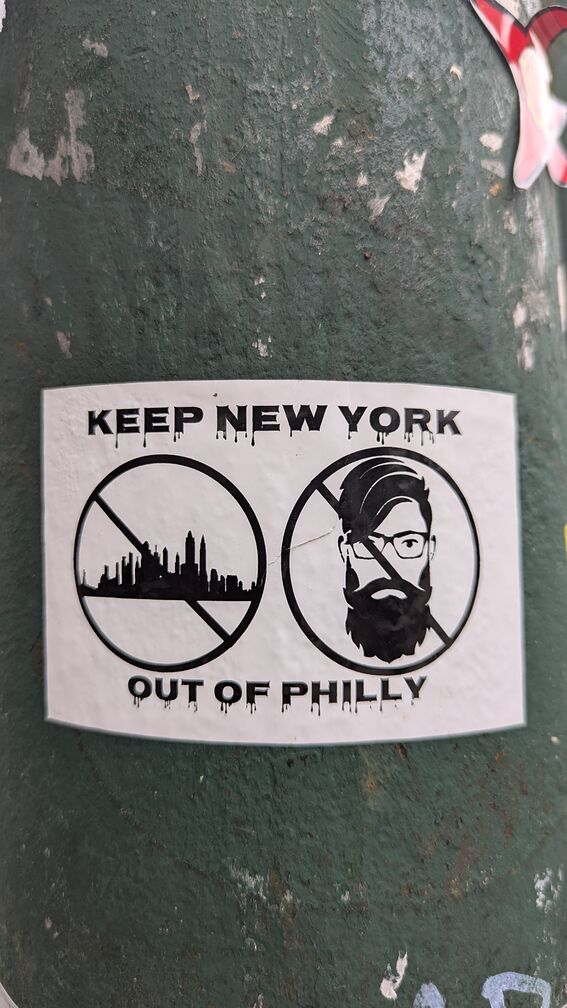 A sticker that reads: Keep New York out of Philly. It has two crossed out circles, one with the NYC skyline in it, and the other with a picture of a bearded bespectacled bohemian. click for full resolution.