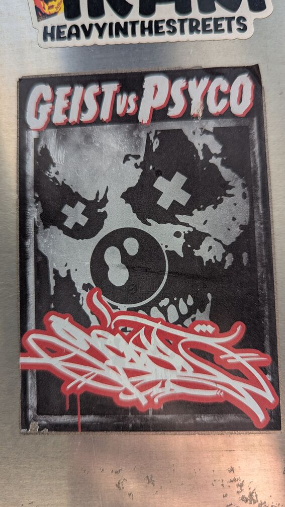 A sticker that says Geist vs Psycho. A demented greyscale clown face image is in the background, and then there's a red graffiti tag above it that I can't quite read click for full resolution.